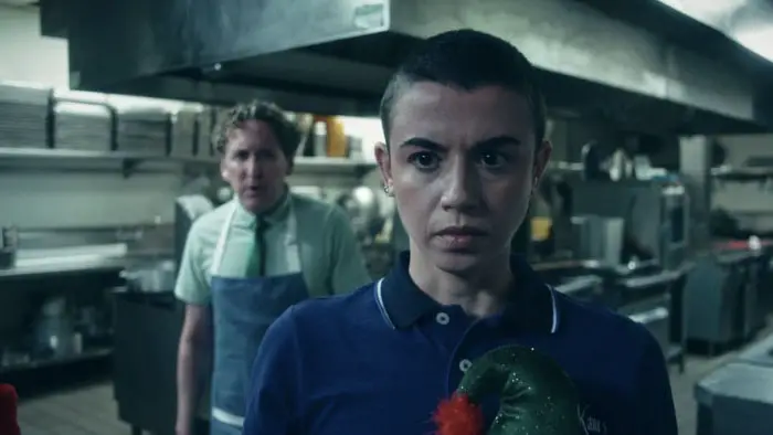 Jenna Kanell as Ashley stands tense in a restaurant kitchen in the Christmas horror-comedy We’re So Dead (2025).