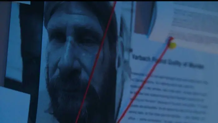 Close-up of a suspect photo pinned to an evidence board with red string in You’re All Gonna Die (2025).