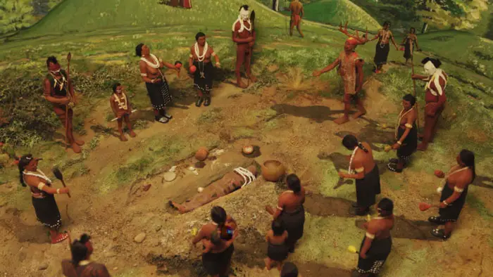 An overhead view of a group standing in a circle around a person lying on the ground during a ceremonial scene in Aanikoobijigan.