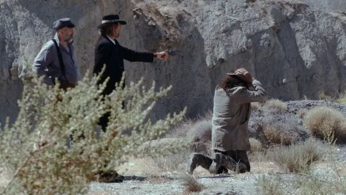 Two armed men hold a kneeling man at gunpoint in the desert in Bullets For The Bad (2026).