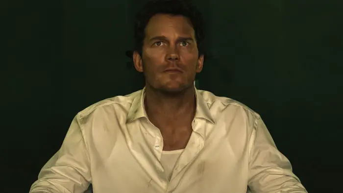 Man in a white dress shirt sits under harsh green lighting in a futuristic courtroom setting in Mercy (2026).