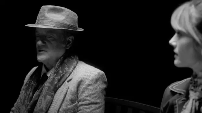 Black-and-white still from No Vacancy showing the Informant speaking while Leigh Larson listens.