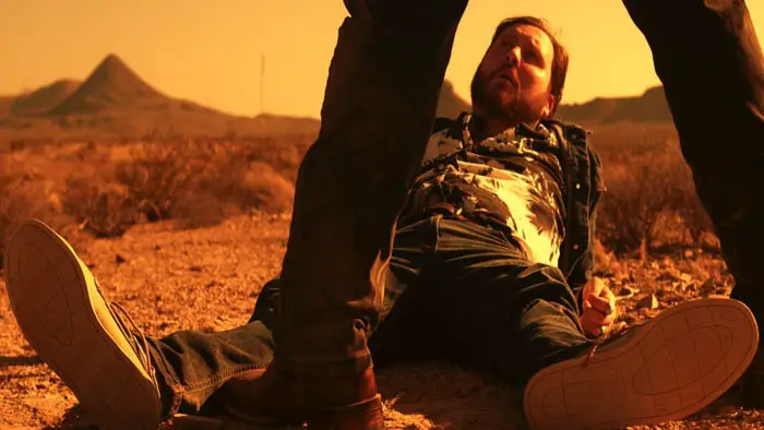 A man lies on the desert ground in Pleasure, Bye during a tense confrontation.