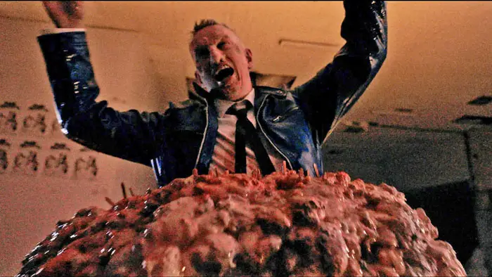 A man in a suit raises his arms while standing on a massive mound of bloody monster flesh in Pulp Modern: Hand of Doom.