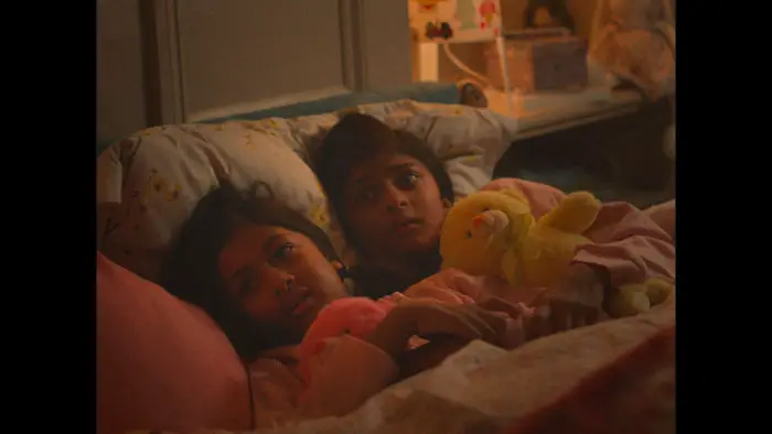 Two children lie awake in bed clutching stuffed animals in There Will Come Soft Rains (2026). 