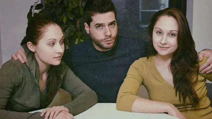 Three characters sit at a table in Videola (2025). 