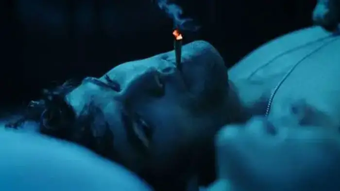 Dark Distortion (2026) still of a person lying in bed under blue lighting with a lit cigarette Title: Dark Distortion (2026) – Blue-lit Bedroom Still 