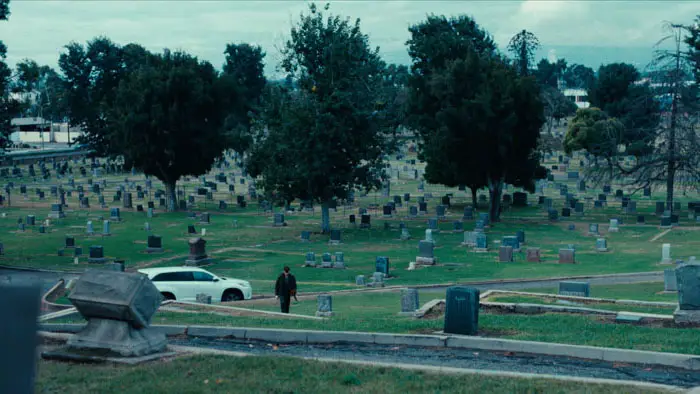 Leonard and Gerald stand apart in a cemetery in Tether (2026), moments before their emotional confrontation.