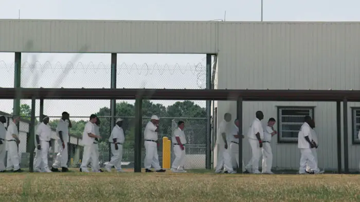 Incarcerated men in white uniforms walk in a prison yard at an Alabama correctional facility